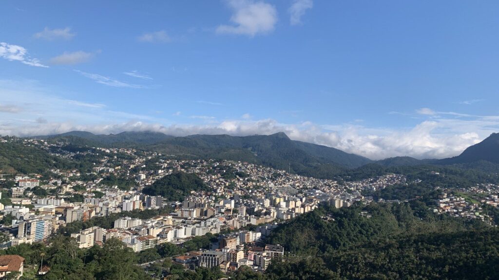 Vista aérea de Nova Friburgo (RJ), com prédios do centro da cidade cercados por montanhas verdes e nuvens ao fundo